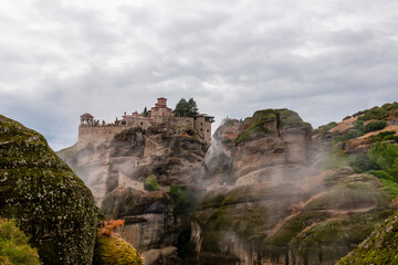 Scenic view of Holy Monastery of Varlaam on cloudy foggy day, Kalambaka, Meteora, Thessaly, Greece, Europe. Rock formations overgrown with green moss creating moody atmosphere. UNESCO World Heritage
