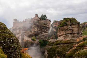 Scenic view of Holy Monastery of Varlaam on cloudy foggy day, Kalambaka, Meteora, Thessaly, Greece, Europe. Rock formations overgrown with green moss creating moody atmosphere. UNESCO World Heritage