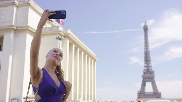 Beautiful young woman in a purple summer dress taking a selfie with the Eiffel Tower behind her
