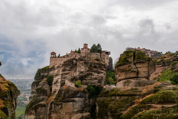 Fototapeta na wymiar Scenic view of Holy Monastery of Varlaam on cloudy foggy day, Kalambaka, Meteora, Thessaly, Greece, Europe. Rock formations overgrown with green moss creating moody atmosphere. UNESCO World Heritage
