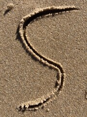 On the beach in the sand is carved the letter S