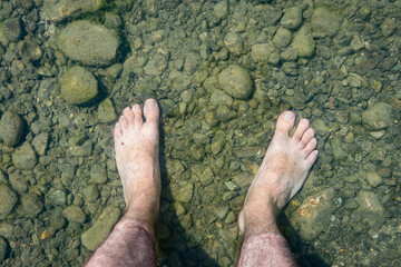 Man's bare feet in clear water. Feet in cold water of a mountain lake. Foot pain on the stones and risk of infections.