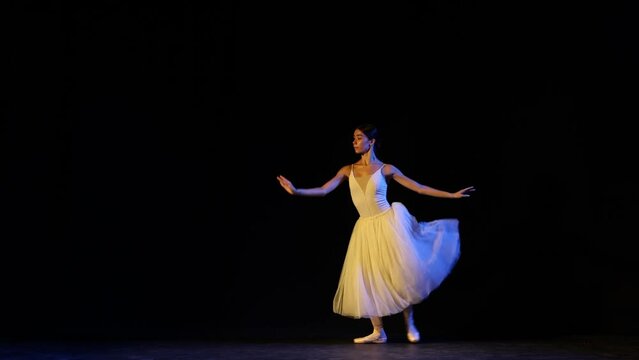Young beautiful woman, female ballet dancer in white dress on pointe doing elements of classical ballet. Looks tender and graceful.