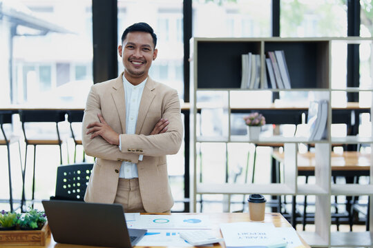 Portrait of a male business owner showing a happy smiling face as he has successfully invested his business using computers and financial budget documents at work