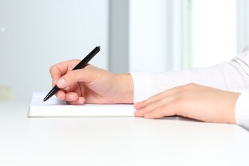 Woman writing in notebook at white table in office, closeup