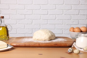 Fresh dough sprinkled with flour and other ingredients on wooden table near white brick wall