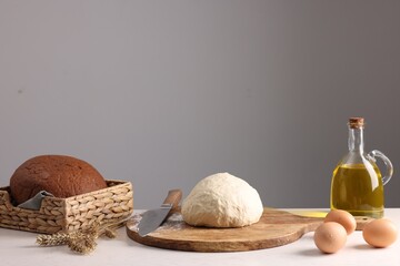 Fresh dough sprinkled with flour and other ingredients on white table near grey wall