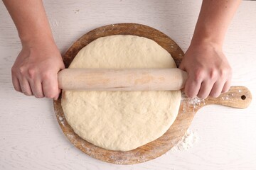 Man rolling dough with wooden pin at white table, top view