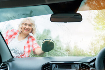 An adult blonde woman washes the windshield of a car with a washcloth, a view from inside the car interior
