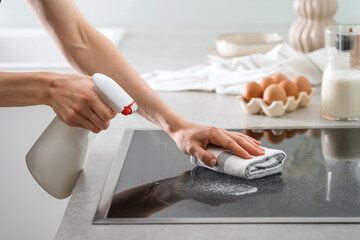 woman cleaning stove surface at home kitchen, closeup