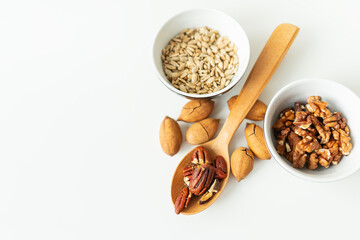 A close-up of a plate with different nuts and seeds along with a wooden spoon lie on a white table. The concept of weight loss, healthy eating, overweight. Fitness menu.