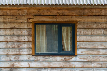 One window on the wooden facade of a rustic house made of wooden beams in a mountains Carpathian village, Western Ukraine, Europe