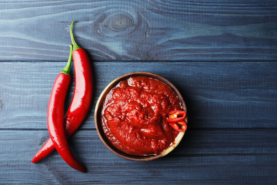 Composition of hot tomato sauce in a wooden bowl on a blue wooden background. Tomato sauce in a wooden bowl, slices of fresh chili peppers, A branch of ripe cherry tomatoes, Fresh allspice basil.