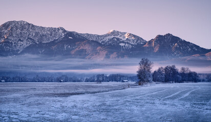Gefrorene Landschaft mit Bergen und Feldern im nebligen Morgenlicht an einem kalten Wintertag -...