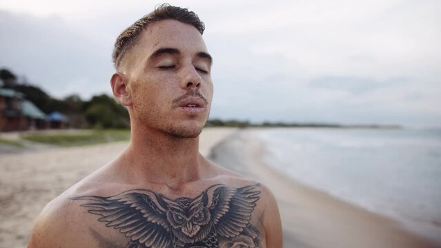 Tattooed shirtless young caucasian man relaxing on beach by sea
