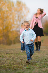 boy runs against the background of his mother and brother, in the autumn park for a walk
