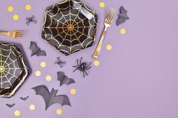 Halloween party flat lay with spider web plates, spiders and confetti on violet background with...