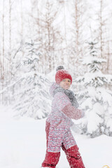 Happy little African-American girl in red hat and jumpsuit walks in the winter forest and throws up snow.Beautiful trees are covered with white snow.Winter fun,active lifestyle concept.Selective focus