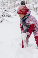 Happy little African-American girl in a red hat and jumpsuit walks in the winter forest.Beautiful trees are covered with white snow.Winter fun,active lifestyle concept.