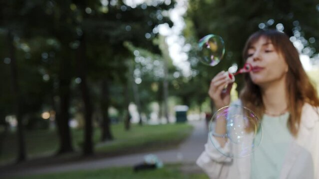 Girl inflates soap bubbles outdoor in park. Golden hour sunset light. Beautiful caucasian young girl.