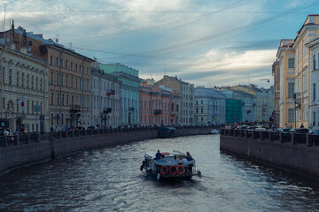 Obraz premium A boat on a river surface against people on an embankment and a Saint Petersburg cityscape by summer day