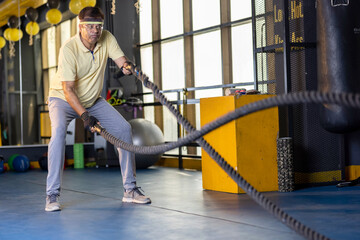 Obraz premium Active old man in sportswear training with battle rope in cross fit gym 