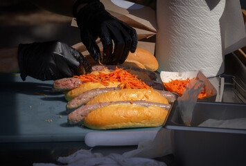 Hands of the cook stack the sliced carrots on a bun with sausage. Street food