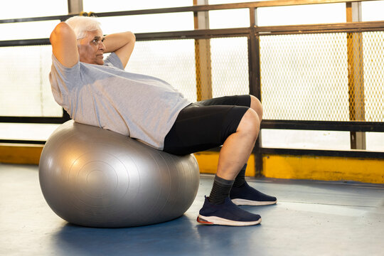 Fit senior man stretching on exercise ball at gym
