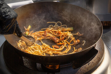 Cooking noodles with meat and vegetables in a deep wok over an open fire. street food