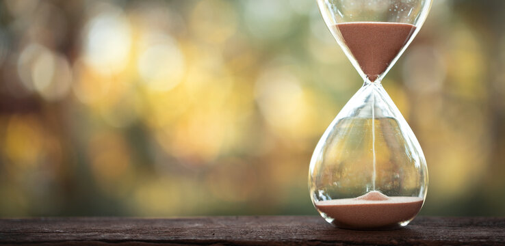 hourglass (sand clock) on an old wooden table with natural blur background, Hourglass as time passing concept for business deadline, Life-time passing concept, elapsed time concept, copy space.