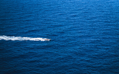 Speed boat racing through the blue sea, leaving a white wake behind it