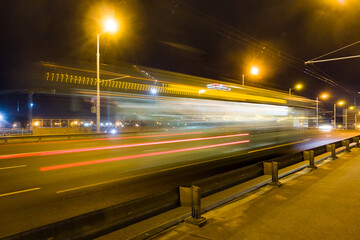 Naklejka na ściany i meble A blurred bus moves along the overpass in the evening..