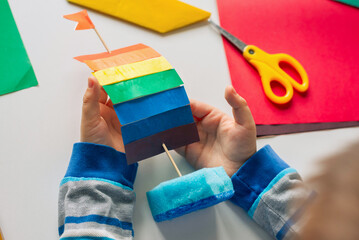 Child Makes a Sailboat out of Sponge and Colored Paper with a Rainbow flag. Family and School Education of Children Concept.