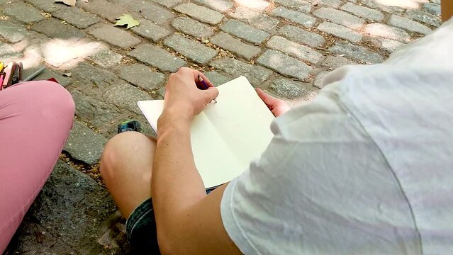 person drawing on the ground in the street on his sketchbook - left handed street artist doing urban sketching