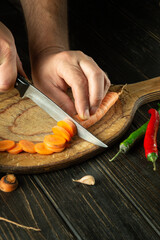 The chef cuts carrot on a cutting board for cooking ajika. Peasant delicious food