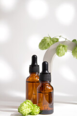Bottles with serum in arch with fresh hop cones. Hyaluronic acid oil, serum with collagen and peptides skin care product. Mockup packaging, cosmetic design branding