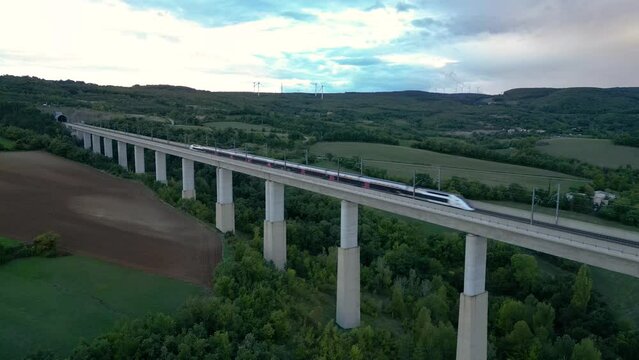 Passenger train crossing the railway flyover and entering the tunnel near La Roche-Sur-Grane (Drome - France). Overlooking the wind farm on the hill