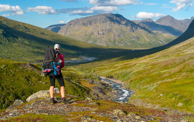 Female hiker with heavy backpack and gear walking in mountain valley in remote Arctic on sunny...