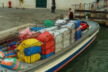 Cargo boat with multi-colored bags at the edge of the street in Venice, transportation of goods by water transport on the Venetian streets, cargo transportation in the city of Venice © Oleksandr Bochkala