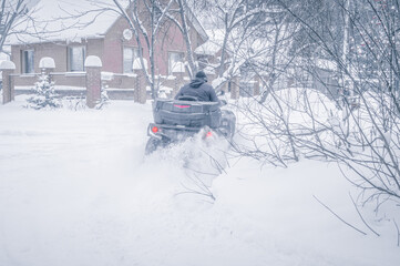 A man rides an ATV on a snow-covered road in the village. Riding in winter in the snow. Selective focus