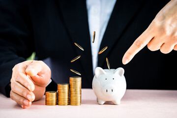 Businesswoman save with dropping gold coins with invest to the piggy bank on the desk in the office, Prevent for asset and saving money for buy health insurance and business investment concept.