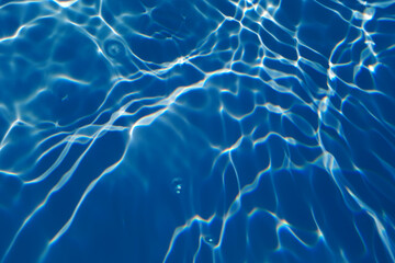 Bluewater waves on the surface ripples blurred. Defocus blurred transparent blue colored clear calm water surface texture with splash and bubbles. Water waves with shining pattern texture background.