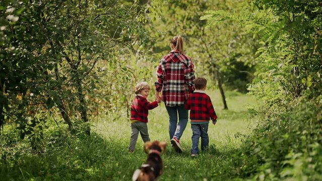 Young family - mom and two brothers twins boys runs with puppy beagle dog in green park or garden. Happy mother and children, love, freedom, future concept