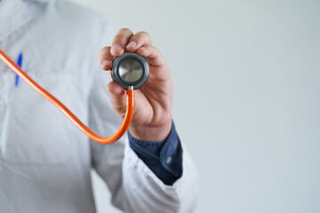 Medical checkup. Doctor hand holding orange stethoscope over grey background