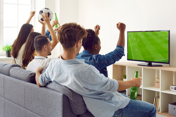 Friends watching soccer match on television. Group of young multiracial people sitting on couch, watching football on TV screen, enjoying free time, drinking beer, raising hands up and cheering loudly