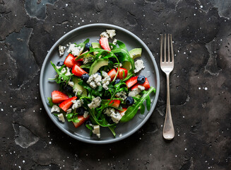 Arugula, strawberry, gorgonzola, avocado salad on a dark background, top view