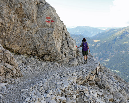 woman with backpack walks on the gravel path in the italian alps