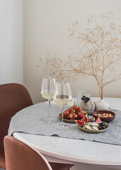 Tapas table - two glasses of white wine, fruit, cheese, nuts in a cozy home environment