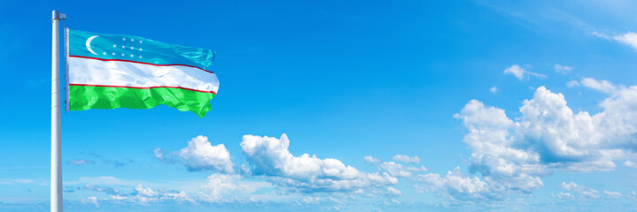 Obraz na płótnie Canvas Uzbekistan flag waving on a blue sky in beautiful clouds - Horizontal banner