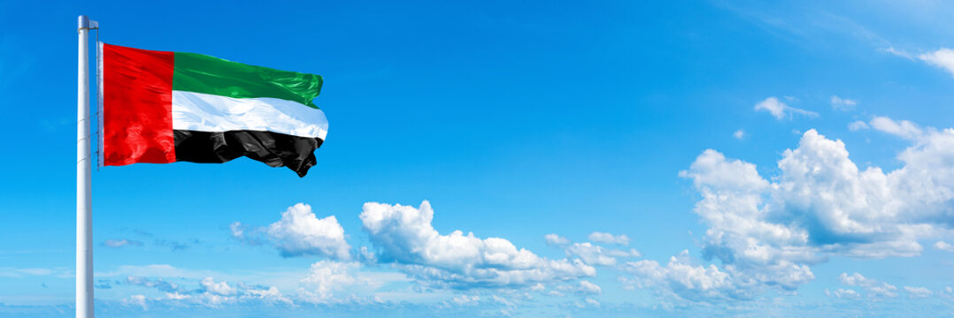 United Arab Emirates flag waving on a blue sky in beautiful clouds - Horizontal banner